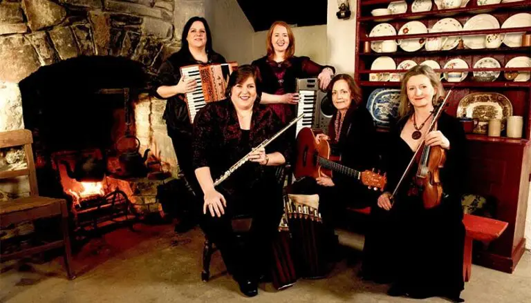 cherish the ladies members with their instruments posing by a stone hearth 768x439