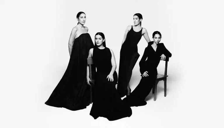 las migas wearing black dresses with a white studio background 768x439