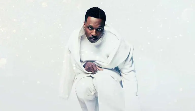 leslie odom jr wearing a white sweater and suit with a snowy studio background 768x439