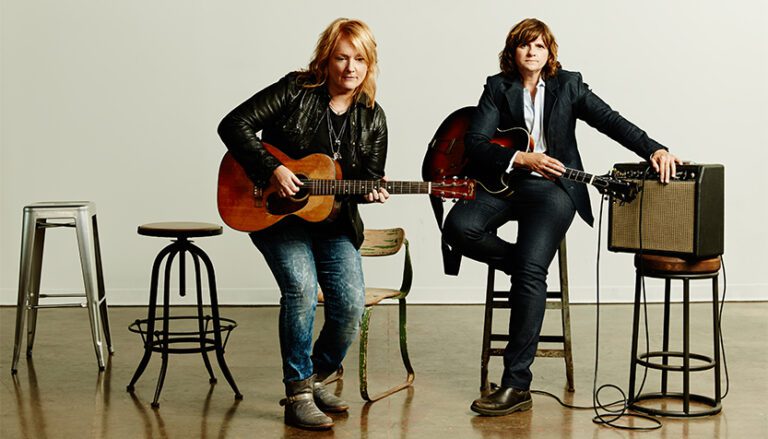 indigo girls wearing black jackets and jeans and holding their guitars 768x439