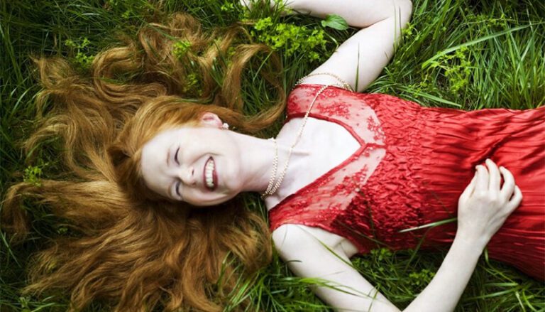 sarah cahill wearing a red dress and laying with her hair spread over the grass 768x439