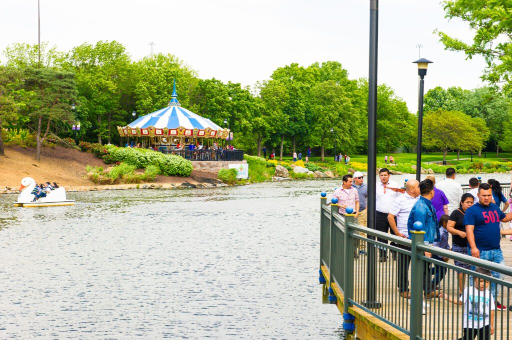 group of people on the boardwalk of rio lakefront with the carousel and people paddling on the paddle boats in the background